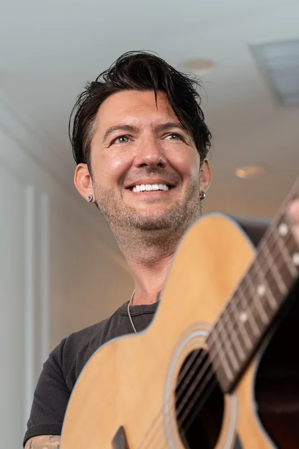 Carl Tomich smiling while holding an acoustic guitar